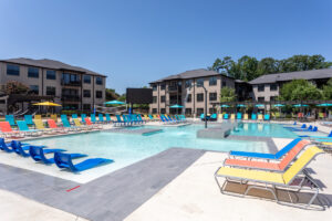 Lark Oxford poolside with apartment buildings in background. Pool is surrounded by lounge chairs in the colors of blue, yellow, and orange. 